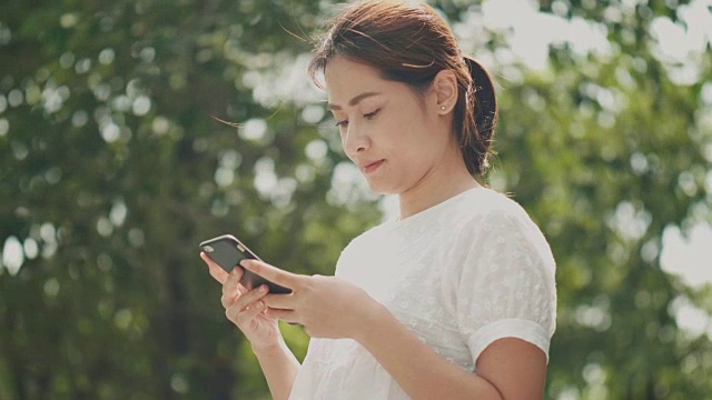 亚洲美女正在使用智能手机上网和聊天的朋友在花园里视频素材