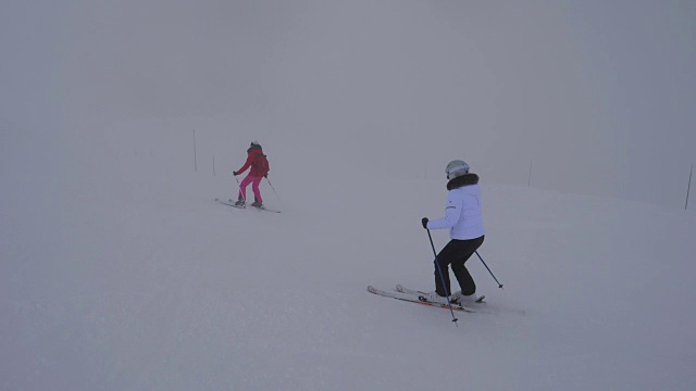 两名女滑雪者在冬季大雾中下坡滑雪视频素材