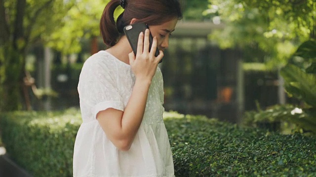 在花园里，一位东南亚美女正在用智能手机和朋友聊天视频素材