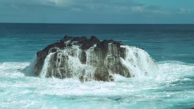 慢动作:泛着泡沫的海水顺着翠绿的海洋中的一块黑色大岩石流下去。视频素材