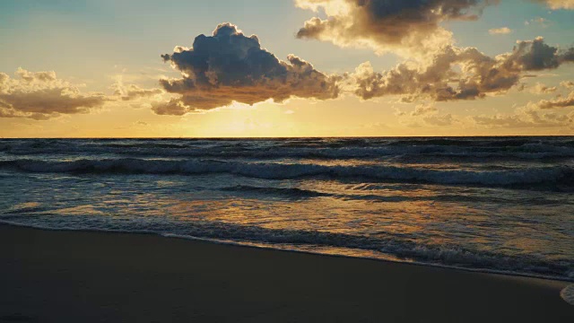 日落在海浪和沙滩上的云后面视频素材