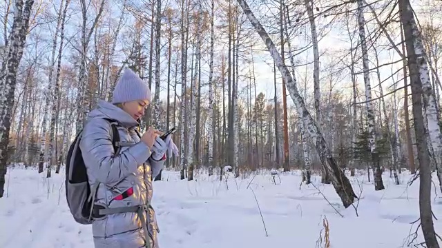 一个女人走在树林里。旅行者在森林里用手机拍照。女孩会自拍，用智能手机交流。美丽多汁的日落时分。视频素材