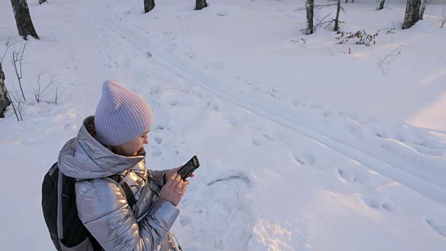 一个女人走在树林里。旅行者在森林里用手机拍照。女孩会自拍，用智能手机交流。美丽多汁的日落时分。视频素材