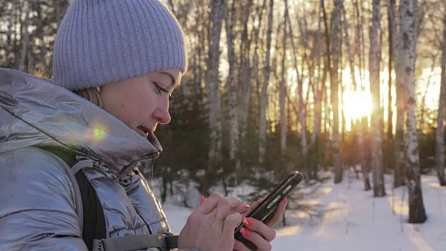 一个女人走在树林里。旅行者在森林里用手机拍照。女孩会自拍，用智能手机交流。美丽多汁的日落时分。视频素材