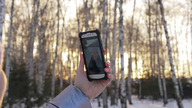 一个女人走在树林里。旅行者在森林里用手机拍照。女孩会自拍，用智能手机交流。美丽多汁的日落时分。视频素材