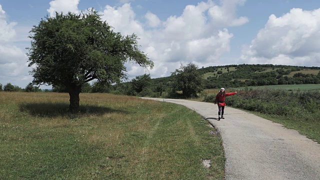 一个徒步旅行的女孩在乡村公路上搭便车的慢动作视频素材