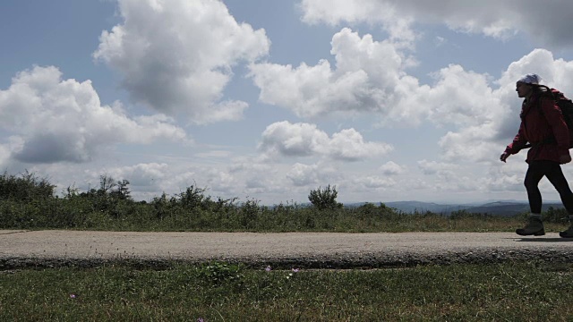 一个徒步旅行的女孩在乡村公路上搭便车的慢动作视频素材