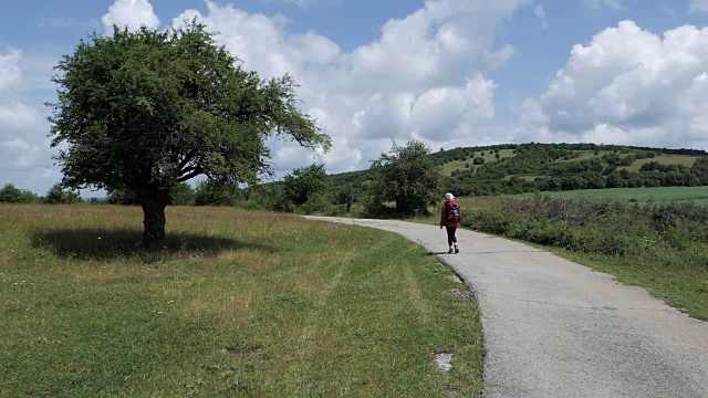 一个徒步旅行的女孩在乡村公路上搭便车的慢动作视频素材