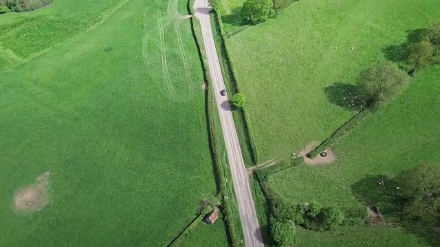 鸟瞰图沿着英国乡村的乡村道路飞行，一辆汽车沿着它行驶视频素材