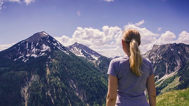 年轻女子举起双手站在背后的山上。视频素材