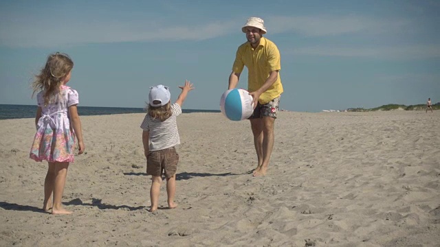 父亲喜欢和小孩子在沙滩上玩球。家庭夏日海滩度假。缓慢的运动。孩子们和爸爸在海滩上玩耍。视频素材