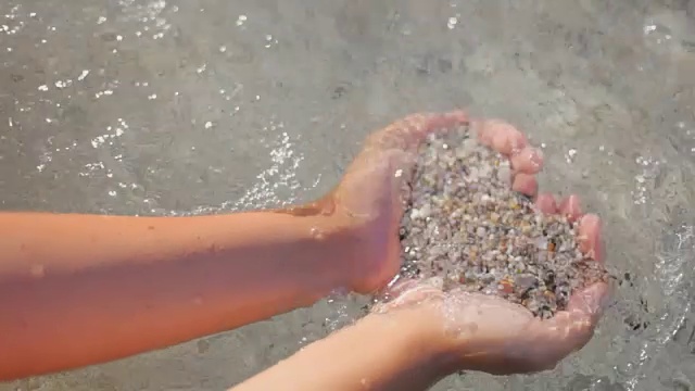 女孩抱着一颗海沙的心，背景是透明的海水。浪漫的夏日假期的概念视频素材