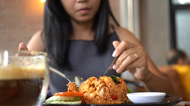 亚洲妇女在餐馆里愉快地吃炒饭。视频素材