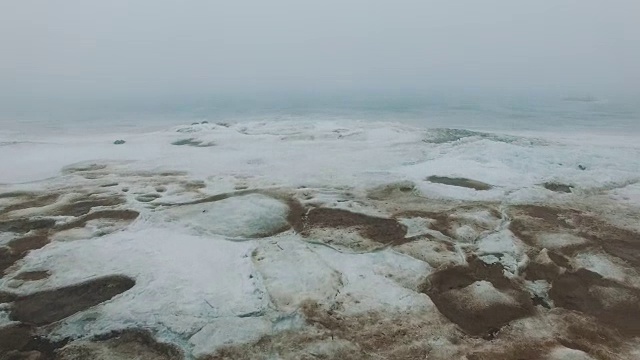 在多雾的寒冷冬日，飞行在有冰裂缝的冰冻海岸线上视频素材