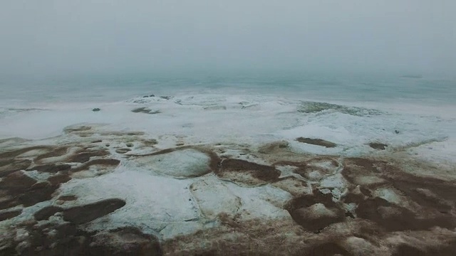 在多雾的寒冷冬日，飞行在有冰裂缝的冰冻海岸线上视频素材