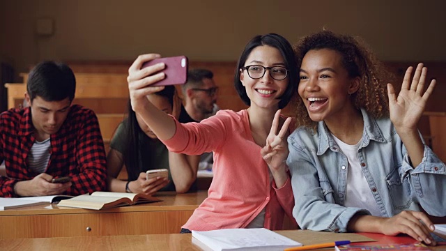 开朗的女学生们坐在餐桌前用智能手机自拍，女学生们摆出手势和拥抱的姿势。朋友与科技理念。视频素材