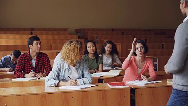 漂亮的年轻女子勤奋的学生正在与高中老师坐在桌子上，而其他学生都在微笑和听。现代教育与青年观念。视频素材