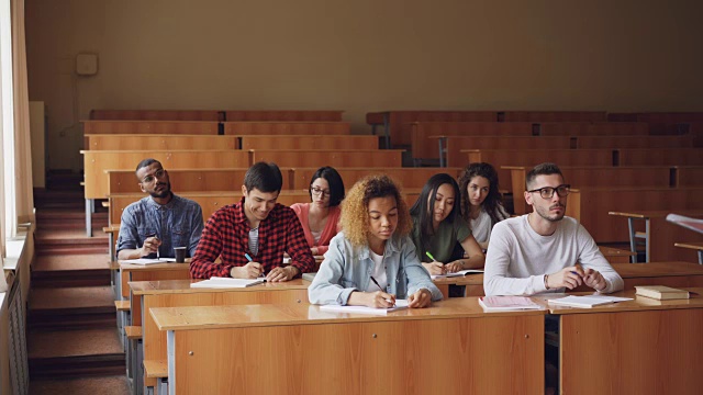 勤奋的学生正在写笔记，在课堂上坐着讲课，而老师是站在他们面前在大教室里。视频素材