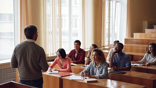 年轻的大学生们正与站在他们面前的友好的教授谈笑风生、打手势。教育和青年观念。视频素材