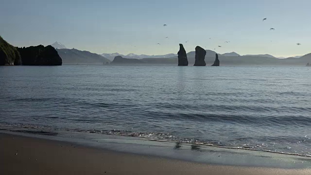 在阳光明媚的日子里，海面上的岩石岛屿和黑色火山沙的海滩视频素材