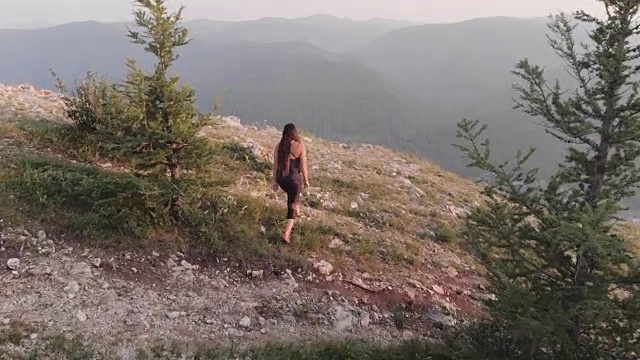 一个年轻的女人走到岩石的边缘，高兴地举起了手。视频素材