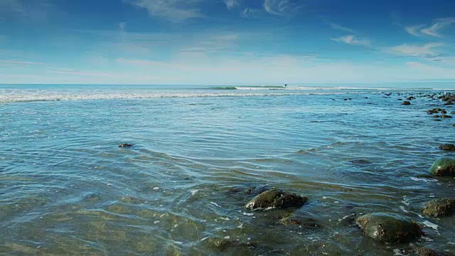 海浪拍打着海滩与远处的冲浪者视频素材