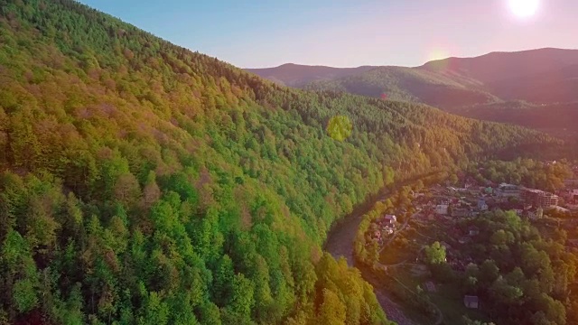 无人机镜头视图:在日出柔和的光线下，飞行在春天的山村与森林。图像处理橙色辉光。喀尔巴阡山脉，乌克兰，欧洲。雄伟的景观。美视频素材