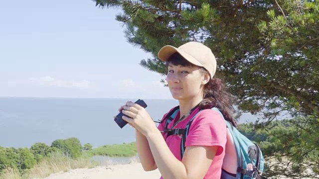 用双筒望远镜观察野生动物的旅行者。女人在度假看自然景观。一个背包旅行者正在用双筒望远镜看大海，看美丽的风景。山。海滩。视频素材