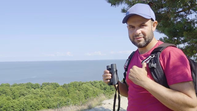 用双筒望远镜观察野生动物的旅行者。男人们在度假中观赏自然景观。一个背包旅行者正在用双筒望远镜看大海，看美丽的风景。山。海滩。视频素材