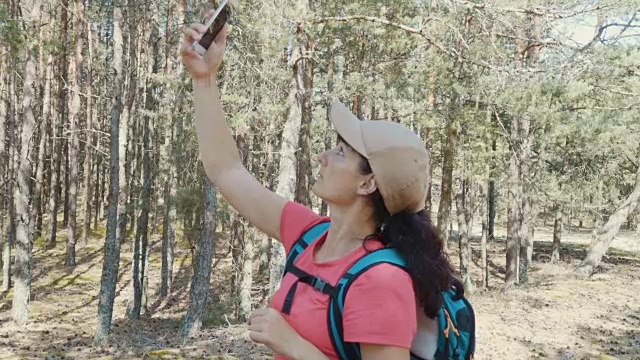 年轻的迷路女人用智能手机在森林里寻找方向。女孩在自然中使用智能手机。徒步旅行者年轻女子背包在夏天的森林。他观察gps地图信号。视频素材