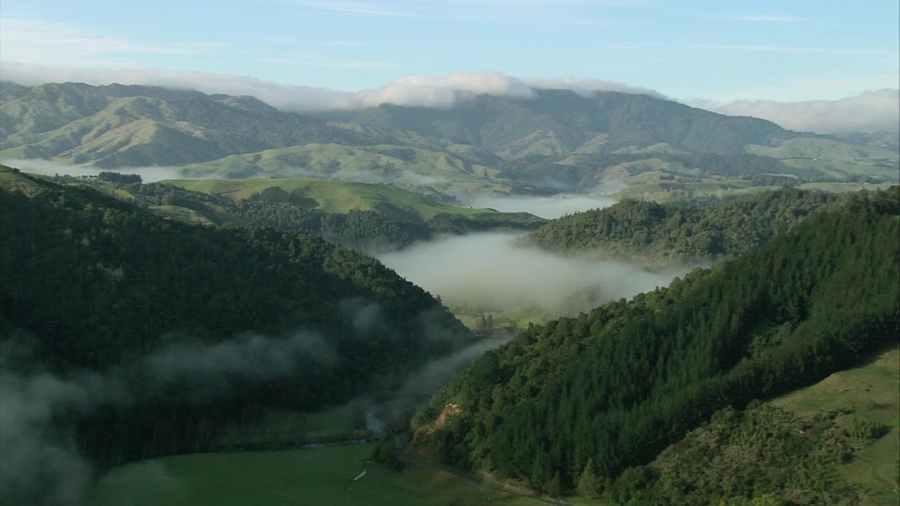 空中的云朵蜿蜒穿过山谷，山峰耸立在郁郁葱葱的绿色森林中，摄于新西兰奥塔哥视频下载