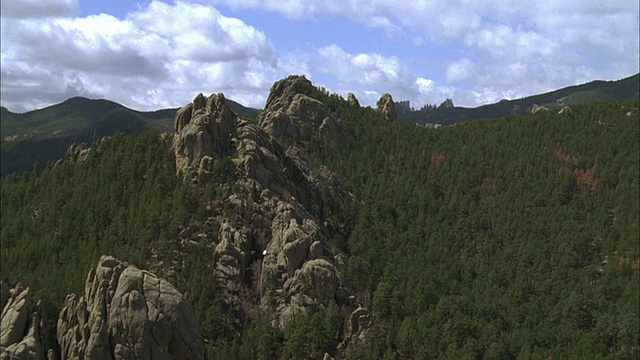 空中飞行在布满岩石峭壁和常青树的山丘和山谷视频素材