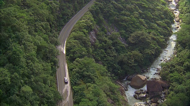 空中双车道公路和河流蜿蜒穿过险峻的森林地带视频素材