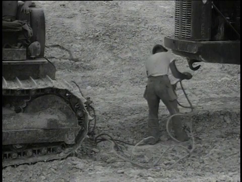 1950年3月1日，建筑工人将一根牵引绳钩在一件重型设备上，向看不见的司机发出移动信号视频素材