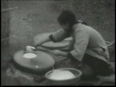 1938年，一名妇女蹲在户外火堆上在大圆煎锅上烤薄饼状的面包/中国视频素材