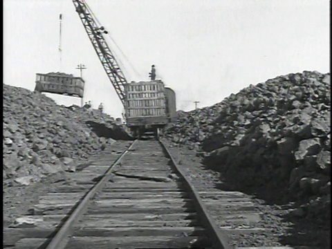 1929年蒙太奇人在炼油厂挖掘和破碎岩石，起重机倾倒集装箱岩石/美国视频素材