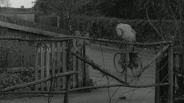 1952蒙太奇灯光在黄昏时分从二楼窗户亮起，地面上的来访者通过楼上的窗户与居民交谈，来访者骑着自行车穿过院子的大门，沿着小路离开/瓦德赫斯特，英国，英国视频素材