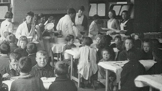 1925年，英国泰恩河上的纽卡斯尔蒙太奇学校的孩子们站在自助餐厅里双手紧握祈祷，穿着白大褂的同学端着午餐，学生们坐在桌前吃着热气腾腾的汤视频素材