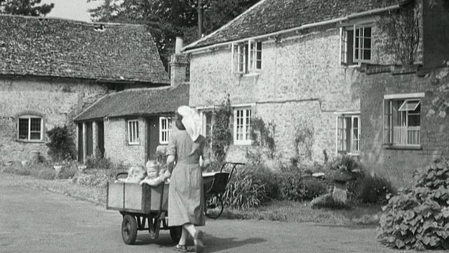 1950年，英国儿童福利院的保姆推着手推车，带着蹒跚学步的孩子穿过大门，转过街角，走下小巷视频素材