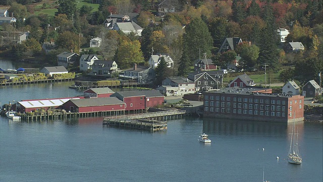 美国缅因州的拜斯港(Bass harbor)，码头上的架空船坞，开放的码头，抛锚的纵帆船，穿过港口的摩托艇，以及小镇上的秋叶视频素材