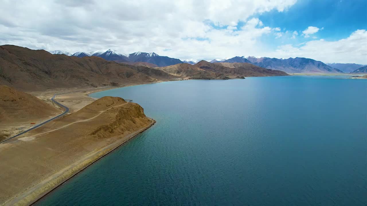 西藏阿里班公湖，六月晴朗的天气，航拍蓝天白云下，湖水湛蓝，雪山环抱，新藏公路从湖边经过。视频素材