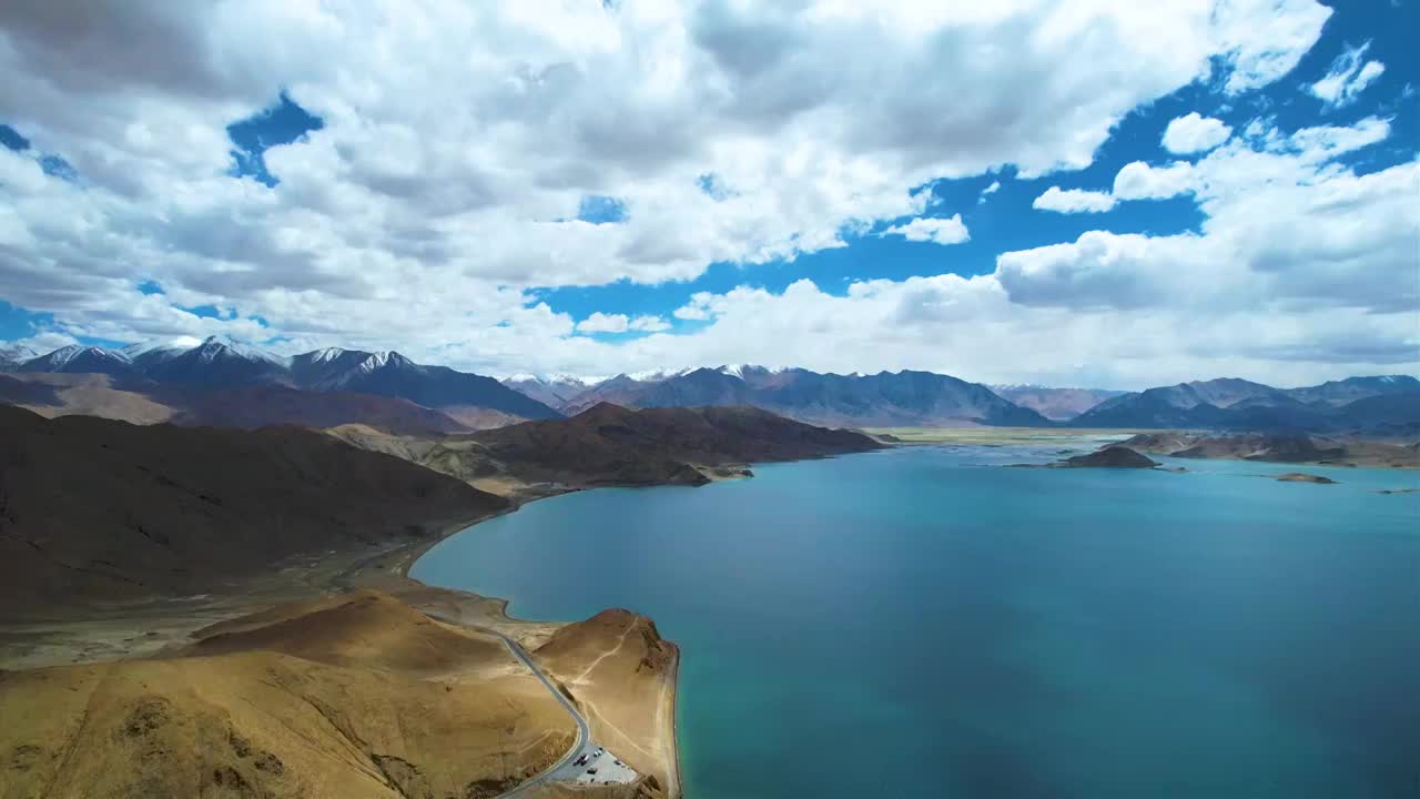 西藏阿里班公湖，六月晴朗的天气，航拍蓝天白云下，湖水湛蓝，雪山环抱，新藏公路从湖边经过。视频素材