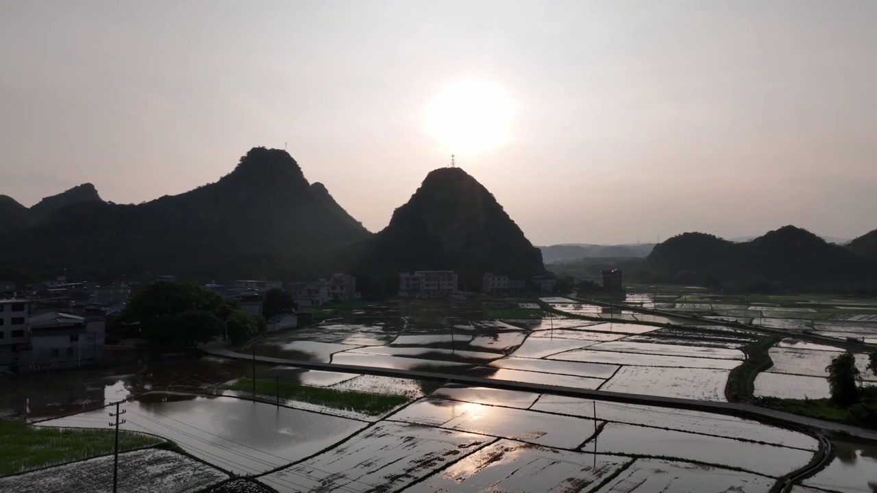 夕阳下山边的村庄和稻田里插秧的农民视频素材