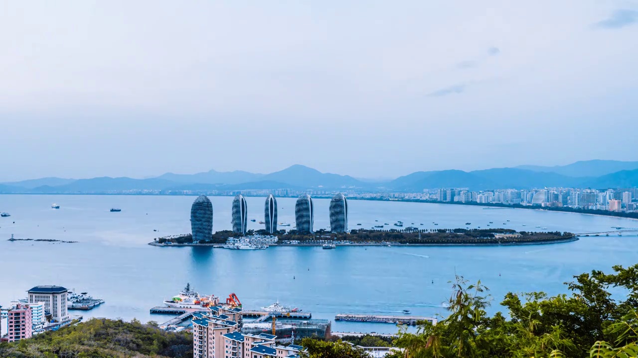 中国海南三亚凤凰岛穿梭的游船和城市天际线日转夜延时摄影视频素材