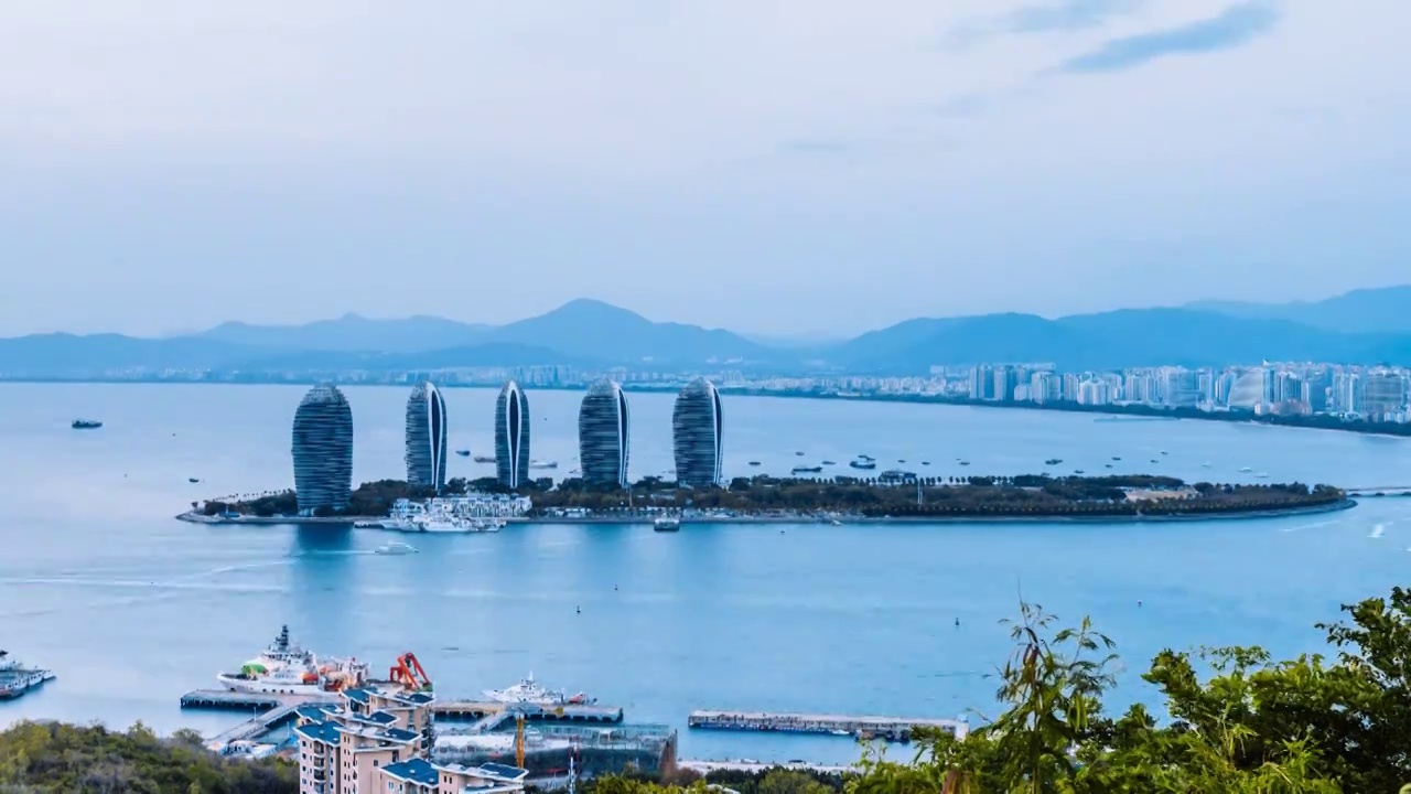 中国海南三亚凤凰岛穿梭的游船和城市天际线日转夜延时摄影视频素材