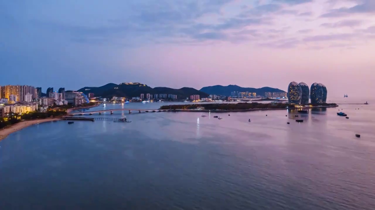 中国海南三亚凤凰岛和穿梭的游艇城市风光夜景延时摄影视频素材