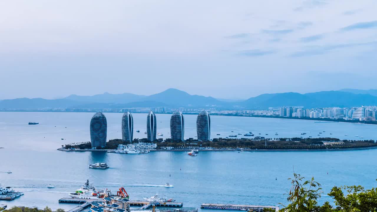 中国海南三亚凤凰岛穿梭的游船和城市天际线日转夜延时摄影视频素材