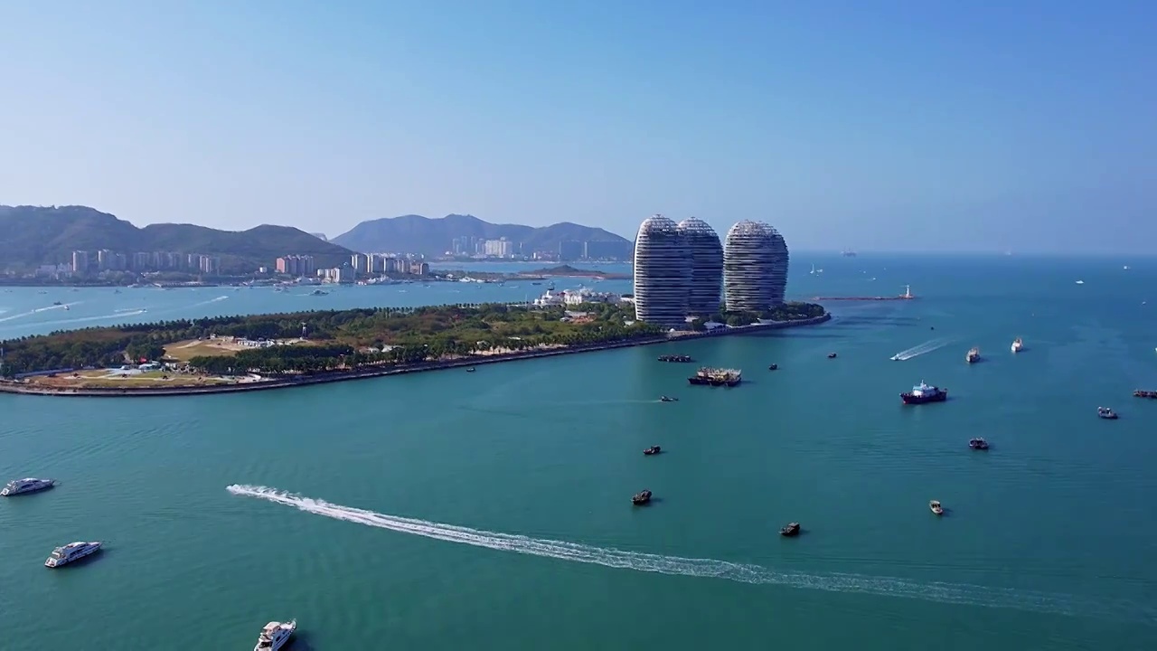 中国海南三亚三亚湾穿梭的游艇凤凰岛和城市天际线风光航拍视频素材