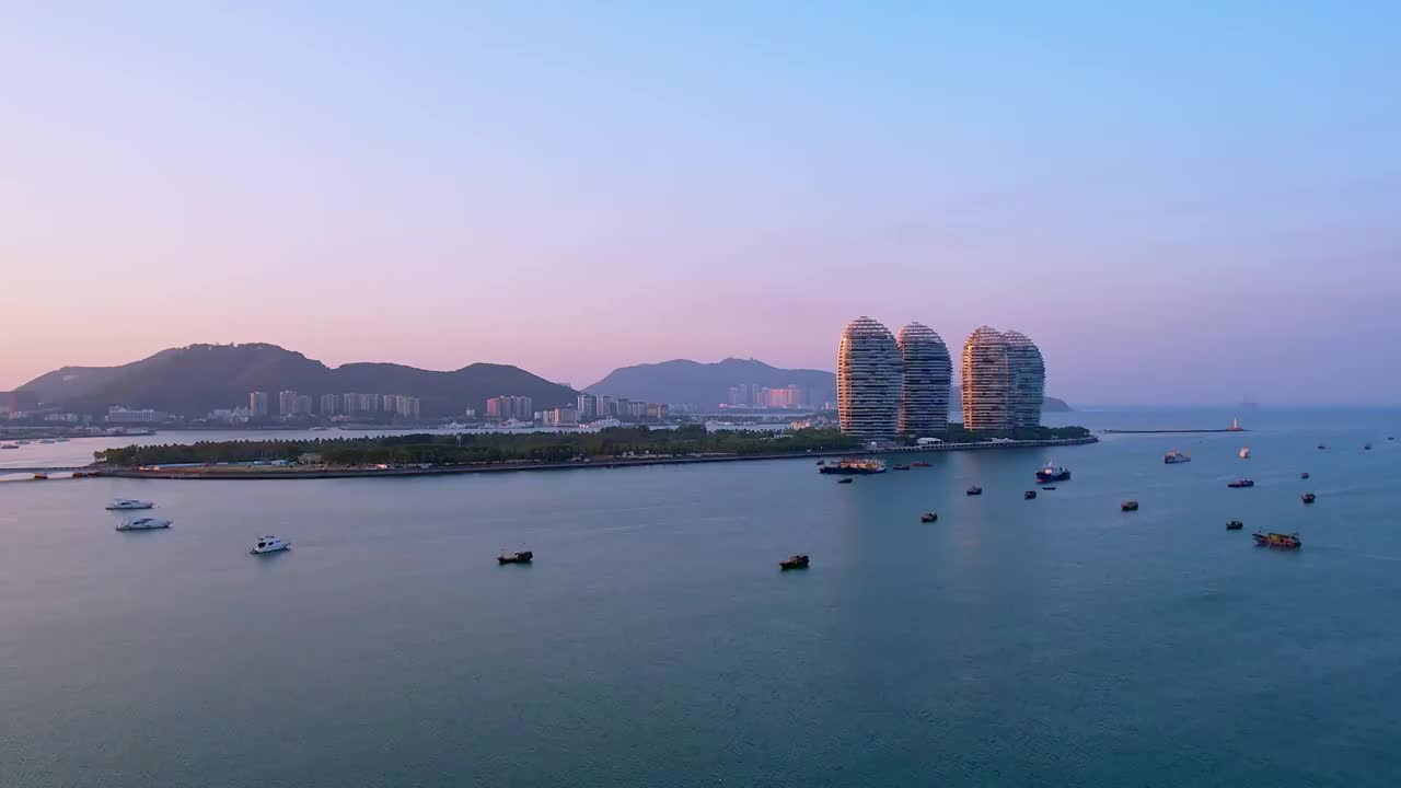 中国海南三亚三亚湾穿梭的游艇凤凰岛和城市天际线黄昏风光航拍视频素材