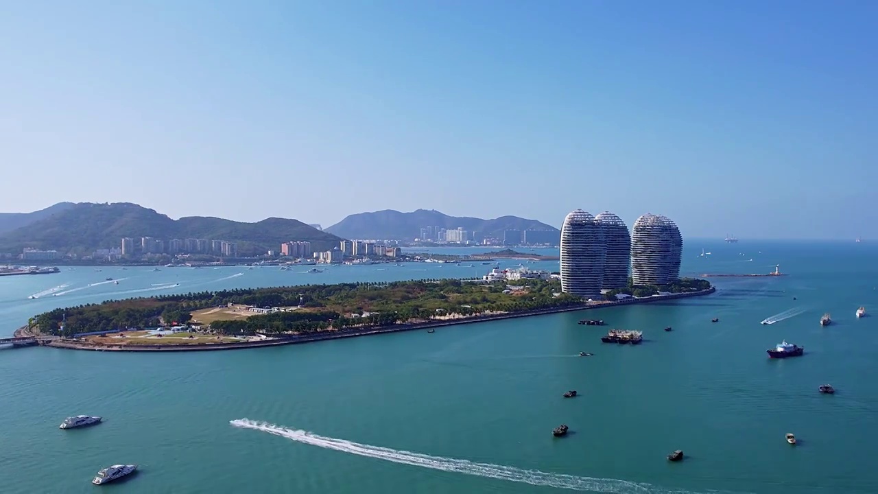 中国海南三亚三亚湾穿梭的游艇凤凰岛和城市天际线风光航拍视频素材